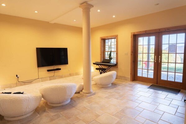 A spacious living room with a large flat-screen TV mounted on the wall, a wooden column, and a sliding glass door leading to an outdoor area.