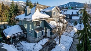 Ein zweistöckiges Haus mit schneebedecktem Dach und Stein Fundament, umgeben von Schnee und Bäumen.