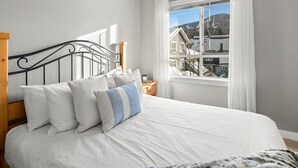 Ein Schlafzimmer mit Bett, einem Fenster mit Vorhängen und Blick auf Gebäude und Berge.