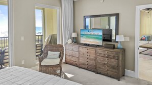 Een slaapkamer met een groot bed, een rieten stoel, een houten dressoir en een televisie waarop 'Legacy Vacations' staat.