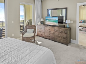 Een slaapkamer met een groot bed, een rieten stoel, een houten dressoir en een televisie waarop 'Legacy Vacations' staat.