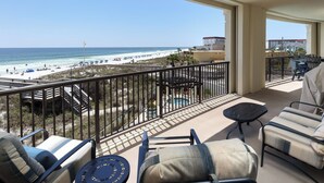 A balcony with outdoor seating, a pool, and a view of the beach and ocean.