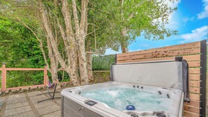 A hot tub in an outdoor setting with a wooden fence and trees in the background. - Seaside Riverfront Escape • HotTub • Walk to Beach (Seaside)