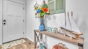 A hallway with a white door, a wooden bench with decorative items, and a wall-mounted mirror. - Seaside Riverfront Escape • HotTub • Walk to Beach (Seaside)
