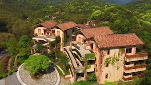 A hillside residential area with terraced houses, some with balconies, surrounded by lush greenery and mountains in the background. - Crosswaters Ecolodge & Spa (Huizhou)