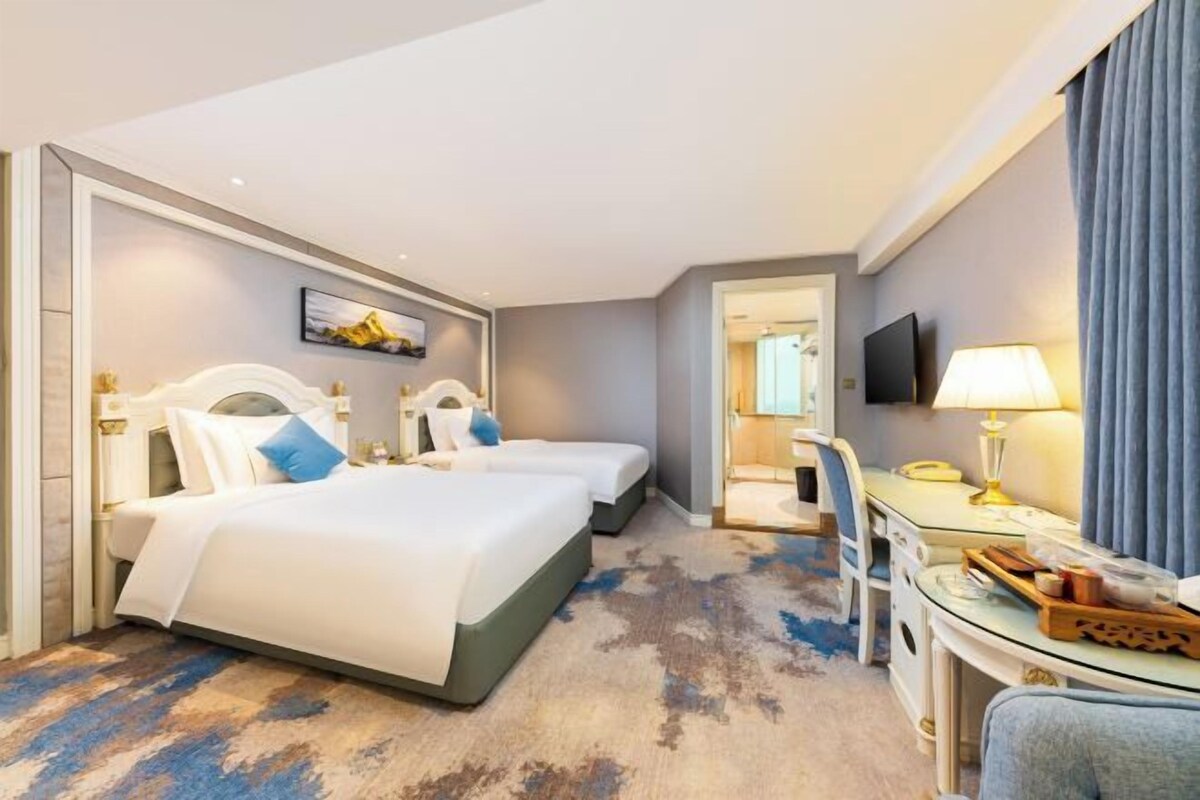 A hotel room with two beds, a desk, a chair, a TV, and a mirror.