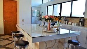 Une cuisine moderne dotée d’un grand îlot central, de tabourets de bar, d’une machine à café et d’un vase rempli de fleurs.