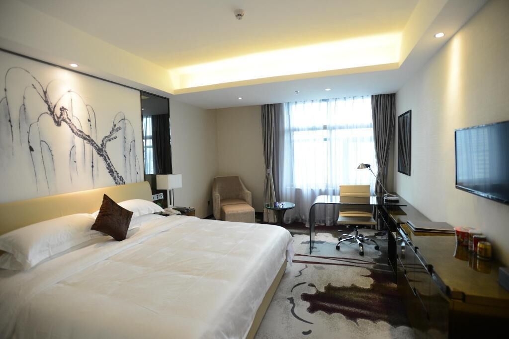 Habitación de hotel con una cama grande, un escritorio, una silla, un televisor y un cuadro en la pared.