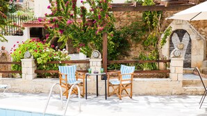 A poolside area with a table and chairs, a stone wall, and a brick oven. - Rousospiti Two Level Villa (Rethymno)