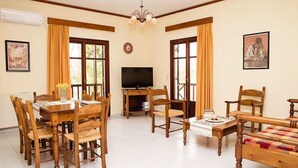 A room with a wooden dining table, chairs, a television, a bed, and a window with curtains. - Rousospiti Two Level Villa (Rethymno)