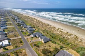 An aerial view of a coastal residential area with houses along the beach, a road, and ocean waves.