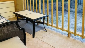Un espace extérieur abrité, doté d’une terrasse en bois, d’une table et d’une chaise.