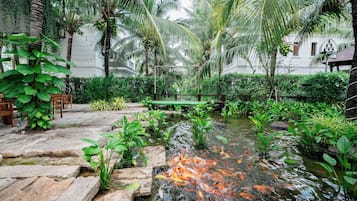 A serene garden with a pond, lush greenery, and a wooden deck.