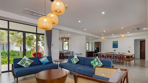 A modern living room with blue sofas, a wooden coffee table, and wicker chairs. There is a dining area with red chairs and a table.