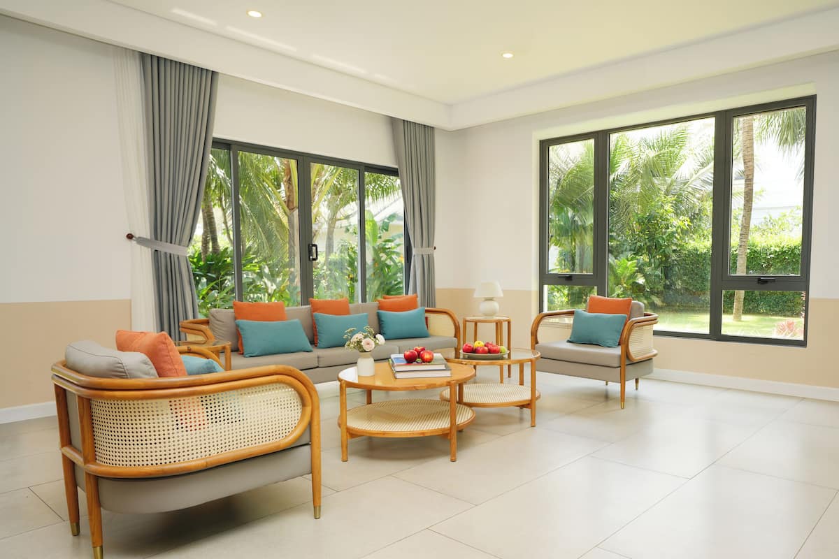 A modern living room with a sofa, two armchairs, a coffee table, and large windows with curtains.