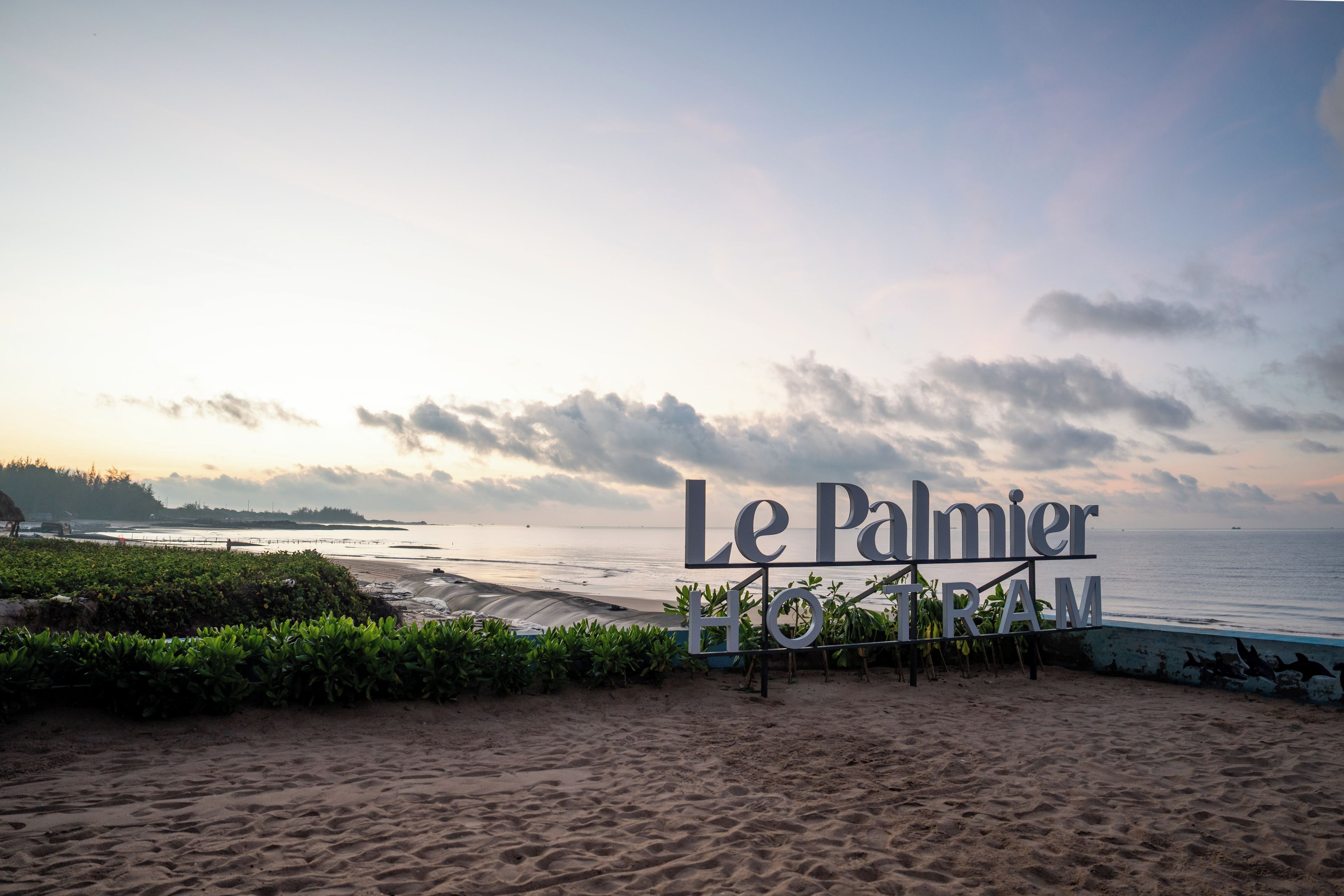 A beach view with a sign reading 'Le Palmier HOTEL TRAM'.