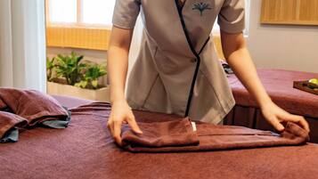A person folding a brown towel on a bed in a room with a window and a plant in the background.