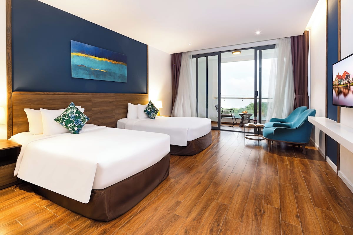 A hotel room with two beds, a balcony with a view, a TV, and a blue chair.