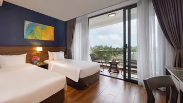 A hotel room with two beds, a nightstand with a lamp, a painting on the wall, and a balcony with a table and chairs.