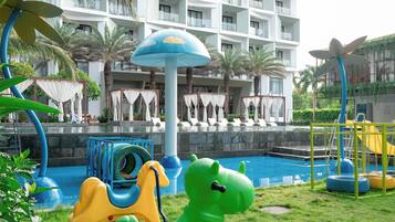 Zona de juegos infantiles con juguetes inflables y piscina, rodeada de palmeras y un edificio de hotel.
