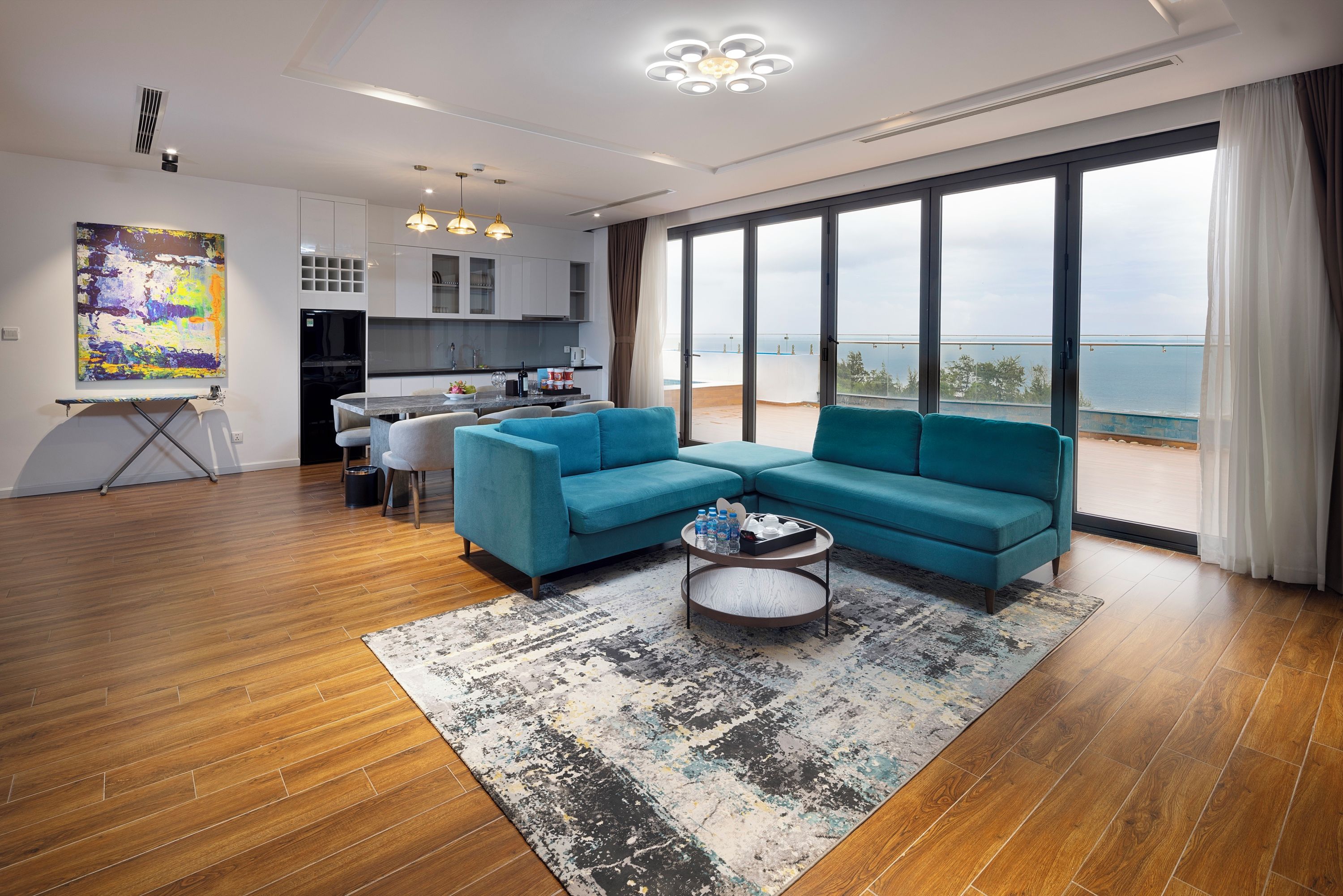 A modern living room with a sectional sofa, a coffee table, and a large window overlooking the sea.