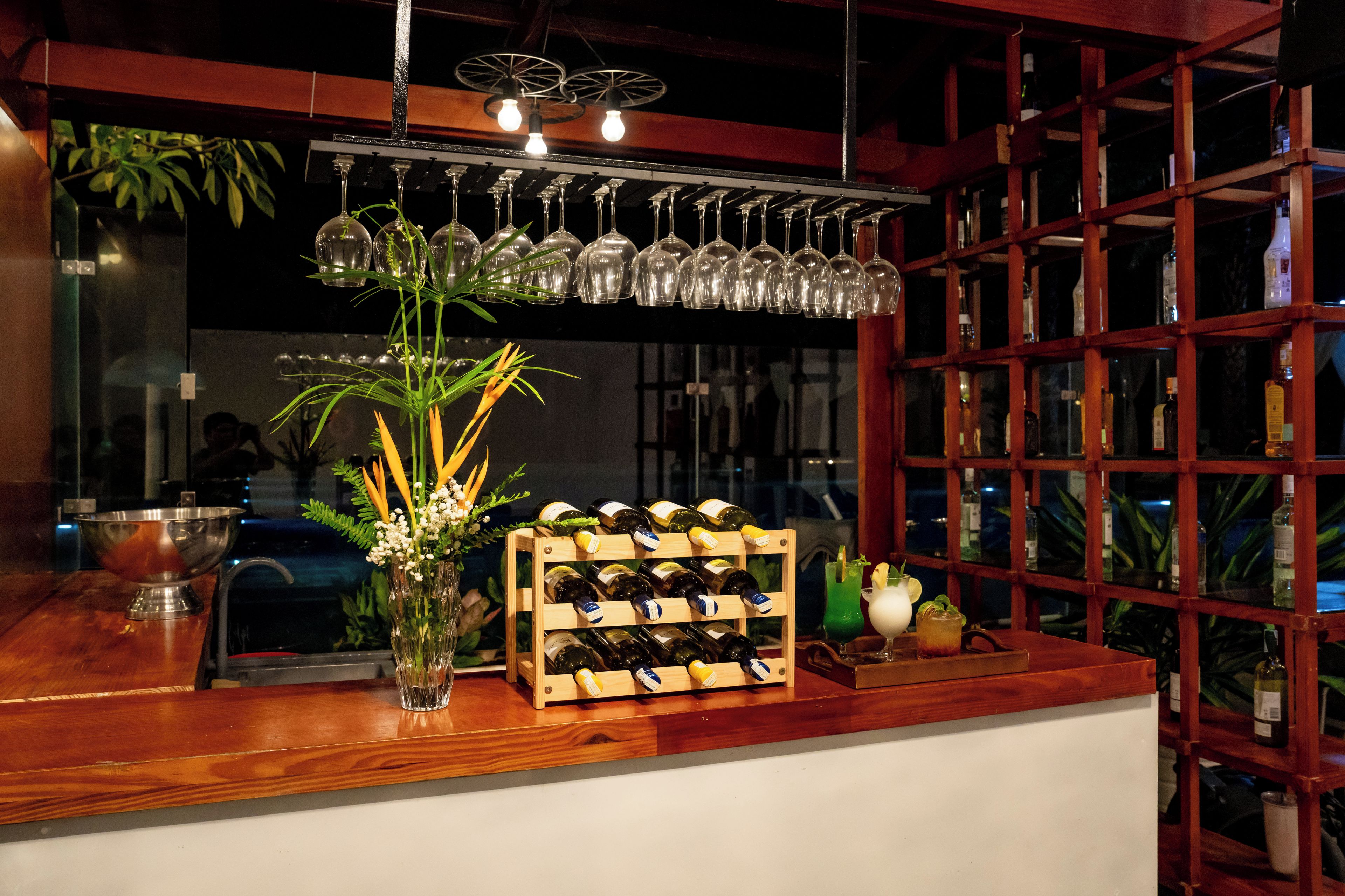 Un coin bar avec un présentoir à bouteilles de vin, un vase rempli de fleurs et des verres à vin suspendus.