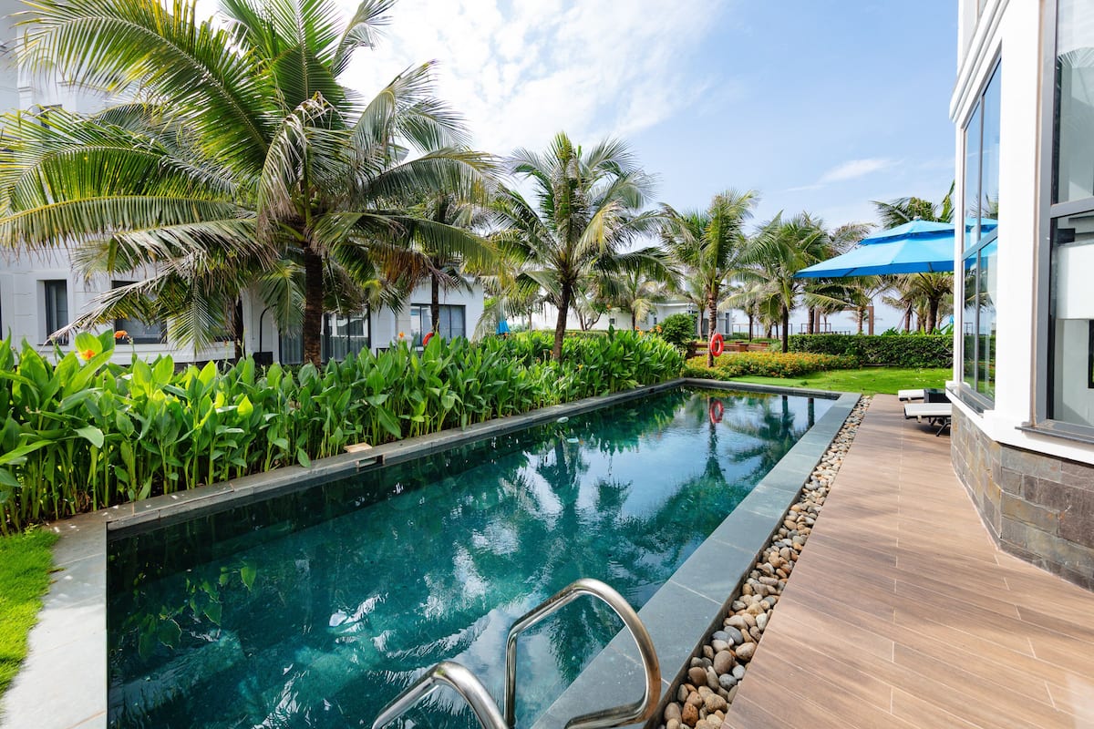 A swimming pool with a clear view of the water, surrounded by palm trees and a well-maintained lawn.