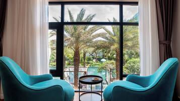 Una habitación con dos sillas color turquesa, una pequeña mesa redonda y un ventanal con vistas a una piscina y palmeras.