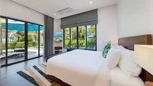 A modern hotel room with a large bed, a view of a pool and palm trees, and a sliding glass door to the outdoor area.
