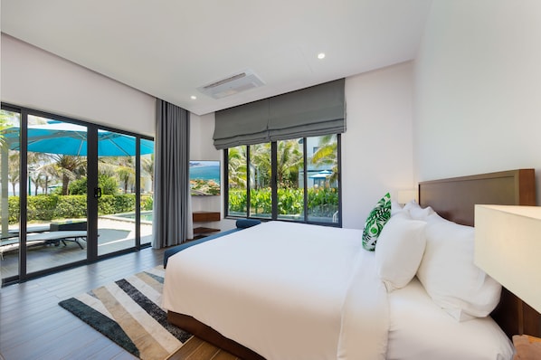 Une chambre d’hôtel moderne dotée d’un grand lit, offrant une vue sur une piscine et des palmiers, et donnant sur l’espace extérieur grâce à une porte-fenêtre coulissante.