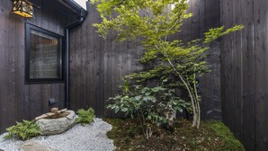 A wooden fence, a small tree, and a stone basin with bamboo sticks.