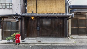 A traditional Japanese building with a wooden gate, potted plants, and a red mailbox.