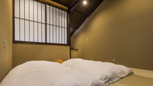 A traditional Japanese-style room with tatami flooring, a low bed with white bedding, a shoji screen window, and a ceiling light fixture.