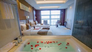 Une chambre d’hôtel dotée d’une grande baignoire remplie de pétales de roses, d’un lit agrémenté de nombreux oreillers et offrant une vue sur la ville grâce à de grandes fenêtres.