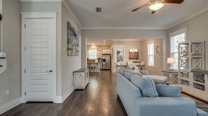 A spacious living room with a light blue sofa, a wooden floor, and a view into the kitchen. - Golf Cart and Bikes Included! Steps Away from the Pool and the Beach! - Anchors Away at Highland Parks (Santa Rosa Beach)