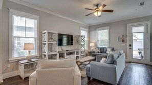 A living room with a sofa, armchairs, a television, and a ceiling fan.