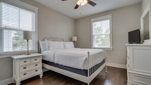 Ein Schlafzimmer mit einem Bett, Nachttischen, einer Kommode, einem Deckenventilator und zwei Fenstern.