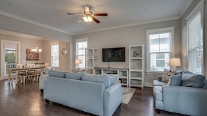 A spacious living room with a ceiling fan, a dining area with a table and chairs, and a TV mounted on the wall.