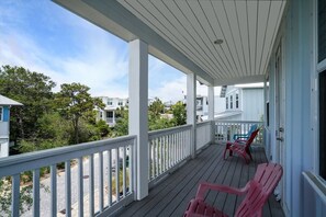 Ein überdachter Balkon mit weißen Geländern und roten Stühlen, mit Blick auf eine Wohngegend mit Häusern und Bäumen.