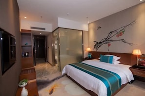 A hotel room with a large bed, a TV, a desk with a lamp, and a wall-mounted artwork. - Ngty Hotel (Foshan)