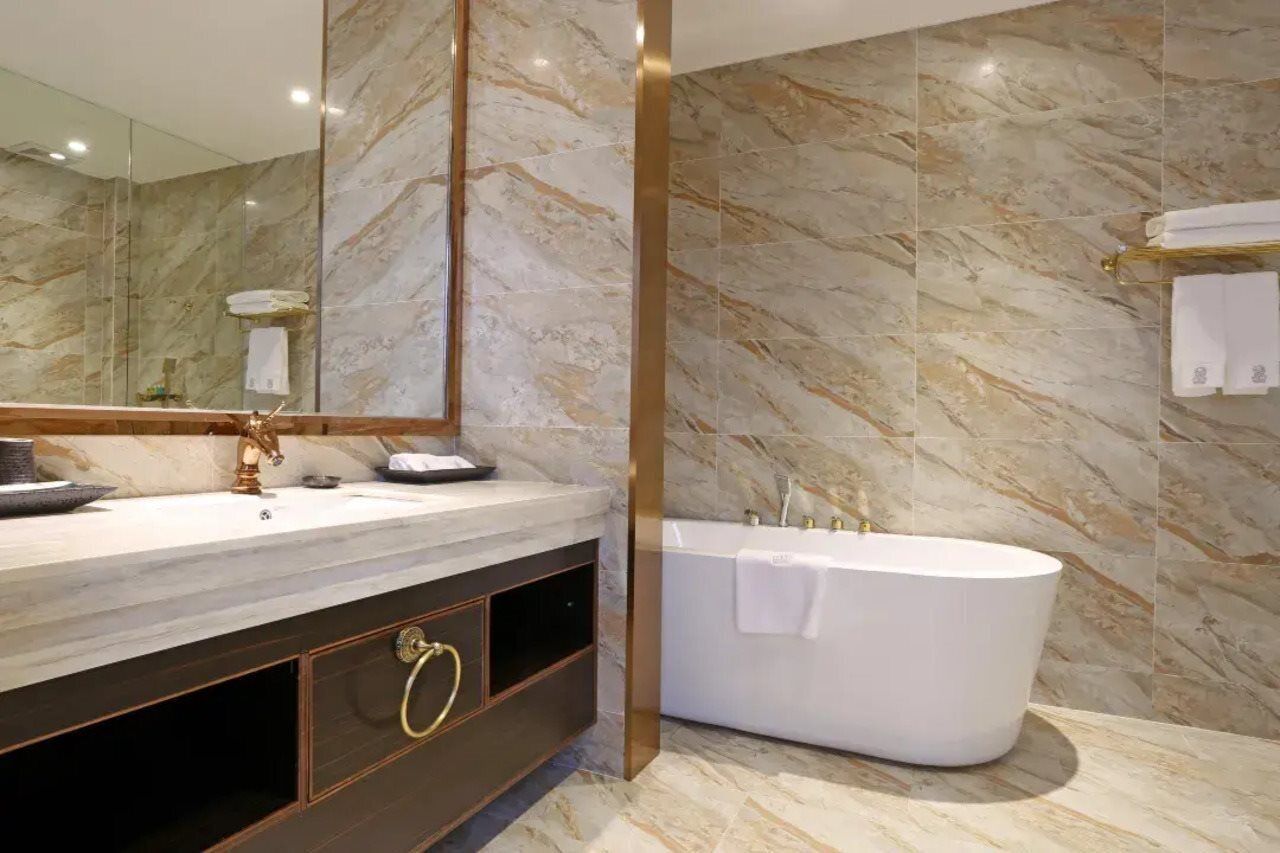 A modern bathroom with a marble wall, a freestanding bathtub, and a vanity with a gold faucet.