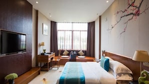 Ein Hotelzimmer mit Bett, Schreibtisch, Stuhl, Fernseher und einem großen Fenster mit Vorhängen.