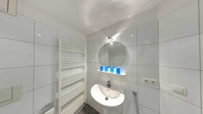 Ein modernes Badezimmer mit weißen Fliesen, einem runden Spiegel, einem Waschbecken und einem Handtuchhalter.