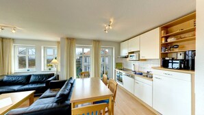 A modern kitchen with white cabinets, a wooden dining table, and a black leather sofa. - Villa Aquamarina Whg. 22, Fahrstuhl, Seeblick - Villa Aquamarina Whg. 22 (Heringsdorf)