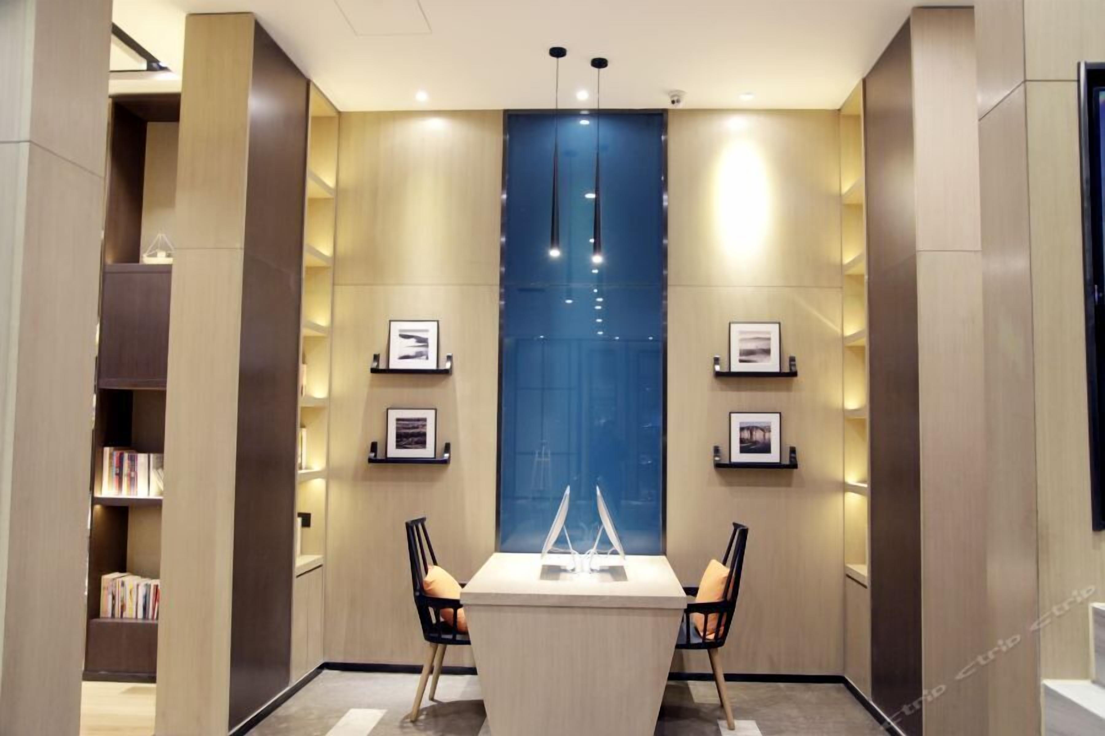 Een moderne hotelkamer met een centrale tafel, twee stoelen, een boekenkast en ingelijste foto's aan de wanden.