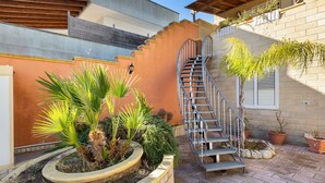 Una escalera de caracol conduce a un segundo piso, rodeada de plantas en macetas y un muro de ladrillo.