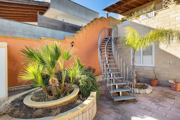 A spiral staircase leading to a second floor, surrounded by potted plants and a brick wall.