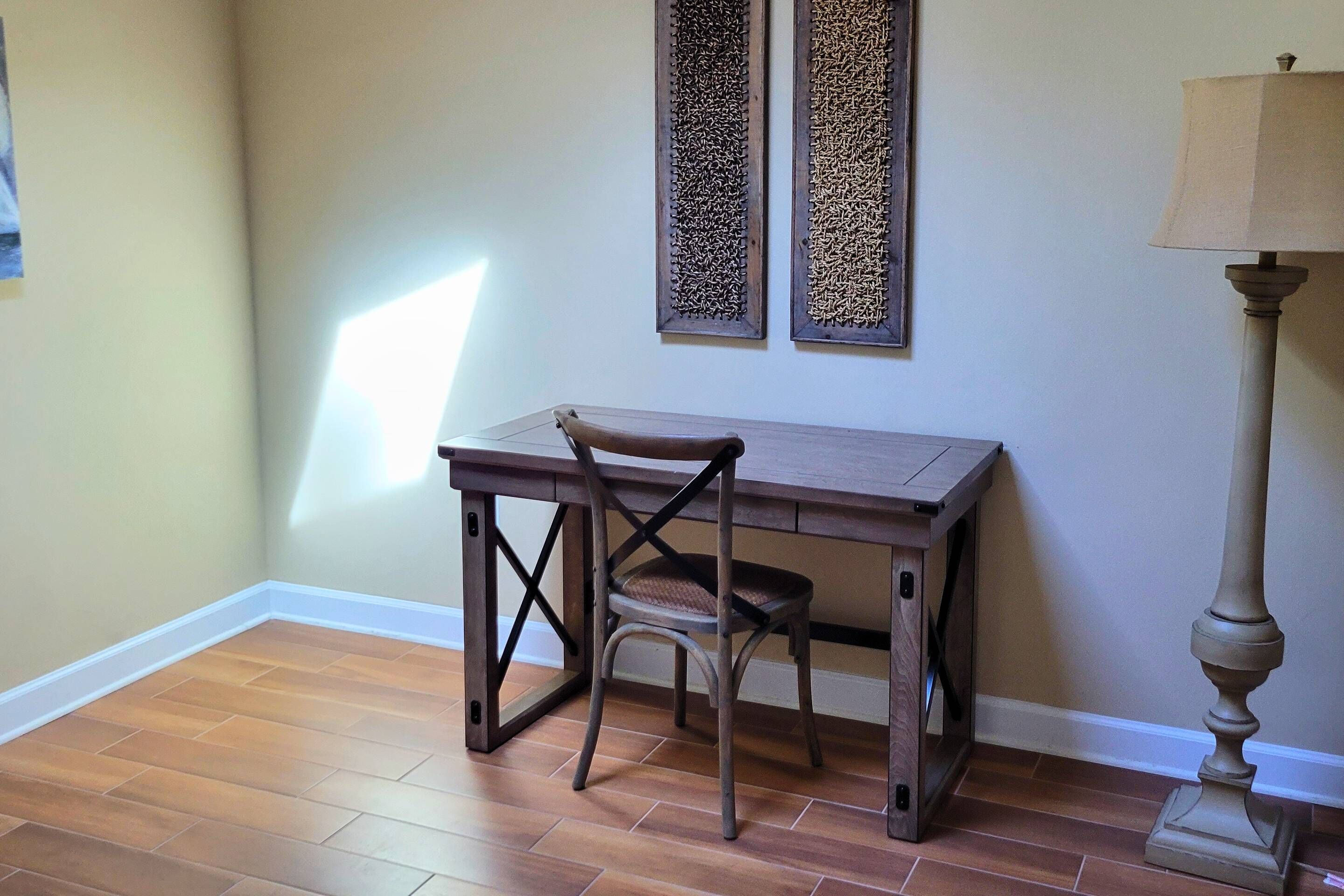 Une pièce d’angle avec un plancher en bois, une table avec une chaise, deux éléments de décoration encadrés accrochés au mur et un lampadaire.