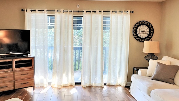 Una sala de estar con una televisión de pantalla plana, un sofá, una mesa de centro y cortinas de gasa.
