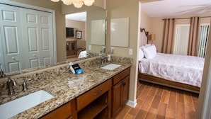 Un baño de hotel con encimera de granito, dos lavabos, un espejo y zona de ducha.